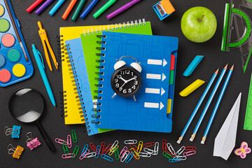 Concept back to school on schedule. alarm clock, notebooks, pencils, student or student tools on the background blackboard for chalk. top view