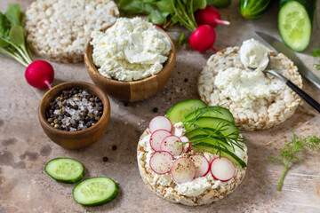 Crispbread sandwiches with ricotta, radish and fresh cucumber on a light kitchen stone or slate countertop.
