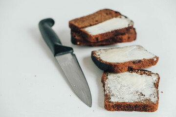 Sliced of brown bread with butter and a kitchen knife on a white wooden background. Top view. Copy, empty space for text