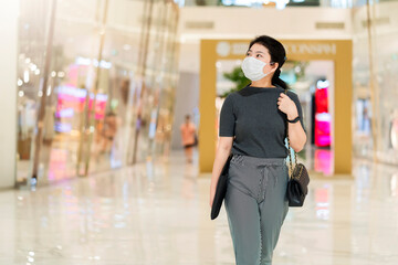 new normal after covid epidemic  young business asian female wear facial protection mask walking in center square department store mall new lifestyle after spread of corona virus covid-19