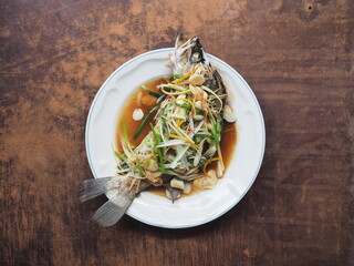 Top view dish of steamed fish in soy sauce with garlic, chili and spring onion on wooden table
