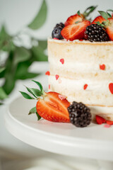 White berry cream cake decorated with strawberries and blackberries, among lilac flowers and green leaves. Food photography. Advertising and commercial close up design.