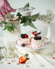 Meringue fruit cake garnished with cream and berries of cherries, blackberries and strawberries, among lilac flowers and green leaves. Food photography. Advertising and commercial close up design.