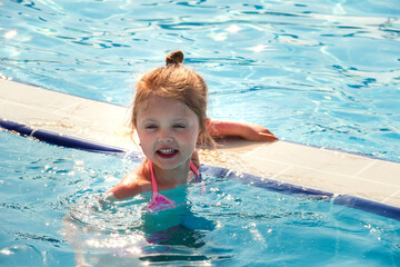 Fototapeta na wymiar A little happy girl swims in the pool in the summer on vacation in the afternoon. A child enjoys the sun
