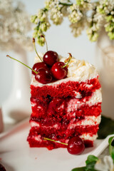 Slised red berry cake decorated with cherry berries and white cream, among lilac flowers and green leaves. Food photography. Advertising and commercial design.