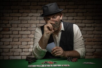 Poker player sitting behind the poker table with cards and playing chips  -  poker in a dark back room with a brick wall