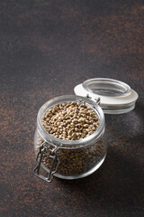 Hemp seeds in glass jar on brown. Vertical. Close up