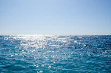 Naklejka na ściany i meble Seascape background of clear sky and vivid blue sea with sunlight reflection on surface