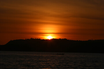 Sunset with the orange sky behind the mountain surrounded by the sea with the dark silhouette 