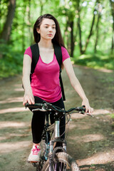 Naklejka premium Girl cyclist in pink t-shirt on a bike on asphalt road in the forest