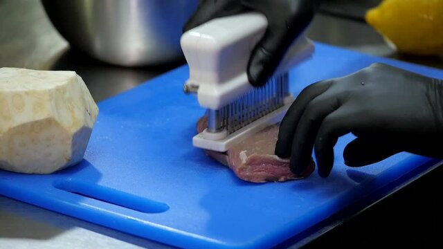 A Piece of Fresh Pork Meat is on a Blue Cutting Board. The Cook Processes the Pork Using a Meat Tenderizer. Pork Chop Cooking in the Restaurant.