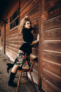 Photo session of a stylish girl outdoors. Young model on a background of a wooden barn.
