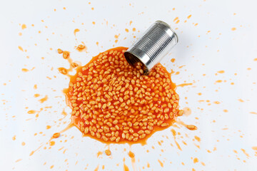 Baked beans splattered in a mess with a tin on a white background. 