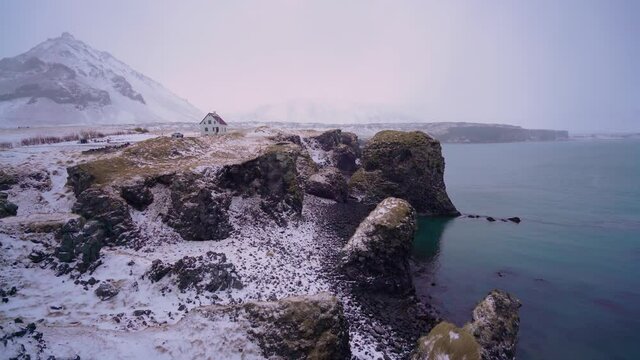 A house is seen overlooking Arnarstapi Harbor on the Sn&aelig;fellsnes Peninsula of Iceland with snow on the ground.
