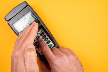 person typing in PIN at POS payment terminal while covering keypad with free hand to prevent spying out of personal data