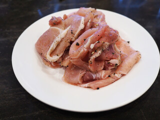 Shabu pork covered with pepper on a white plate placed on a black marble table.