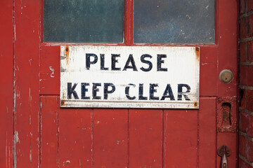 Old and worn hand-painted 'Please keep clear' sign on old worn red door.
