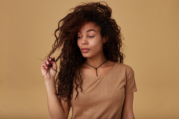 Studio shot of young attractive curly dark skinned female with casual hairstyle pulling her long...