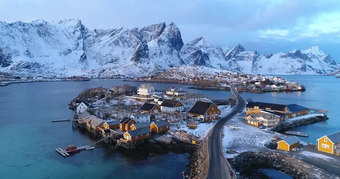 A town on the Lofoten Islands, Norway is seen with snow-covered mountains in the distance.