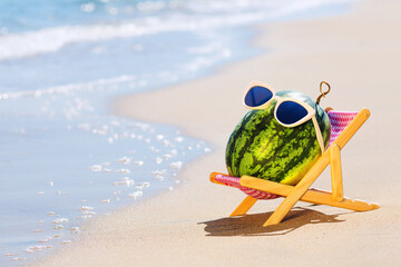 Summer lifestyle image of attractive watermelon lying on sunbed on the sand against turquoise sea....