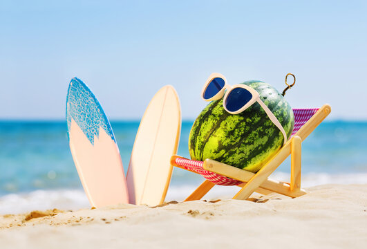 Summer lifestyle image of attractive watermelon surfer lying on sunbed on the sand against turquoise sea. Wearing stylish sunglasses. Surfstyle. Tropical summer vacation concept. Sunbathing on beach
