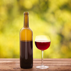 Glass and bottle of red wine unusually on wooden background.