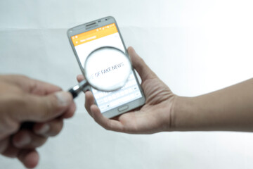 Isolated Hands holding a phone and magnifier with 'fake news" wording in the white background