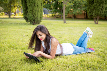 The girl spends time in quarantine outdoors. Young Indian girl lying in the park on the grass,...