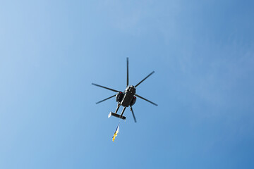 Fototapeta na wymiar Small civil helicopter with Ukrainian flag flies against a blue sky with clouds background