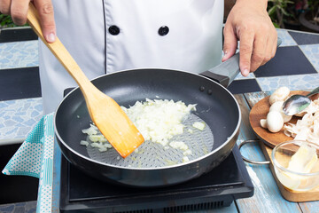 Chef stiring minced onion in the pan prepared for cooking mushroom cream soup