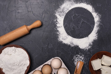 Eggs, flour,butter and rolling pin on a dark background. Free space for text.