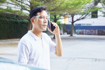 A man is holding a phone outside, wearing a face shield to protect against germs and viruses. Dust prevention and prevention of toxic fumes. Mental Health, Health concept