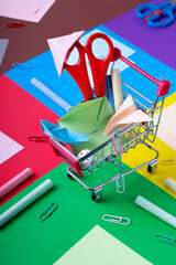 Stationery and multicolored paper origami toys in a little shopping cart against the geometric background