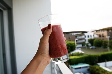 A glass of fruit smoothie in a female hand. View from the balcony