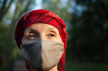 Mature woman wearing handmade textile face mask as accessory and protective element during sunny spring day in the park because of coronavirus pandemic