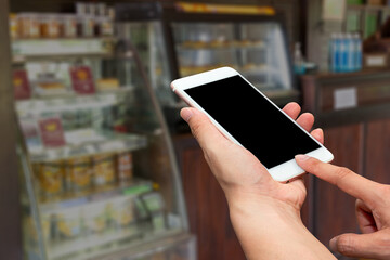 Close up man's hands hold and touch screen smartphone or cellphone with blank black screen for put it on your own webpage or message over blurred coffee shop background