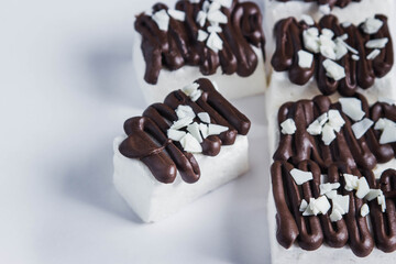White marshmallow poured by dark chocolate. Marshmallows on a white background. Sweet cuisine. Marshmallows closeup