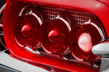 Rear cluster of an old timer luxury sports car with three tail lights with red and white glass...