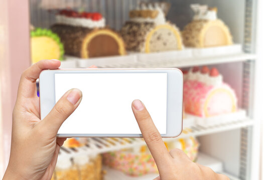 Close up women's hands hold and touch screen smartphone or cellphone with blank white screen for put it on your own webpage or message over blurred cake in refrigerator background
