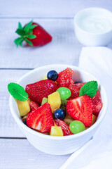 Fruit salad of grapefruit, strawberries, kiwi, mango, grape and blueberry on white dish. Vertical orientation