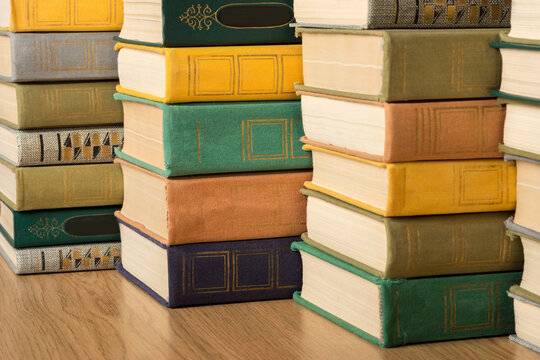 A stack of multi-colored old hardback books and textbooks on a shelf in a library.