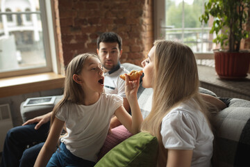 Mother, father and daughter at home having fun, comfort and cozy concept. Looks happy, cheerful and joyful. Beautiful caucasian family. Spending time together, drinking tea, eating croissant, icecream