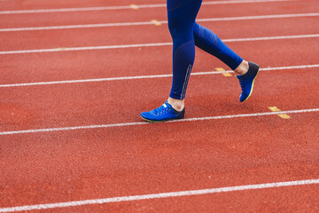 Young fitness woman in blue shoes and blue leggings walking on running court or treadmill. Girl in...