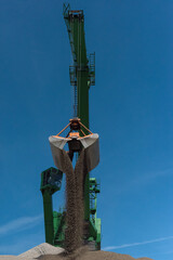 Green harbor crane pours sand and gravel onto a hill