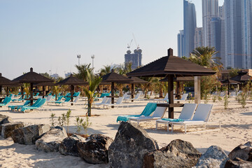 White sun loungers under brown wooden umbrellas stand on the beach