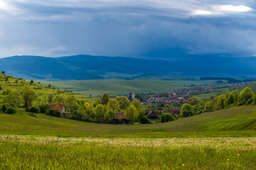 Small , hungarian transylvanian village at sunset with gathering stormclouds in Romania.