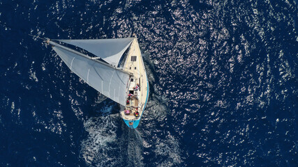 Aerial drone top down photo of beautiful sail boat cruising deep blue Aegean sea
