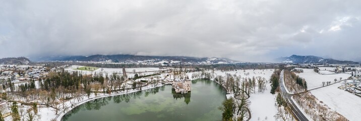 Panoramic aerial view of Schloss Anif moated castle in pond at Salzburg outskirts in heavy snow during winter with view of untersberg snow mountain
