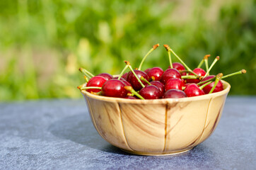 Ripe red cherries hang on the handle of a basket on a background of nature. The concept of gardening.