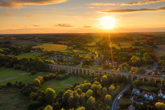 The railway viaduct at Chappel and Wakes Colne in Essex, England the sun a gold ball just above the horizon casting rays light and shadows across the landscape making the tops of the trees glow